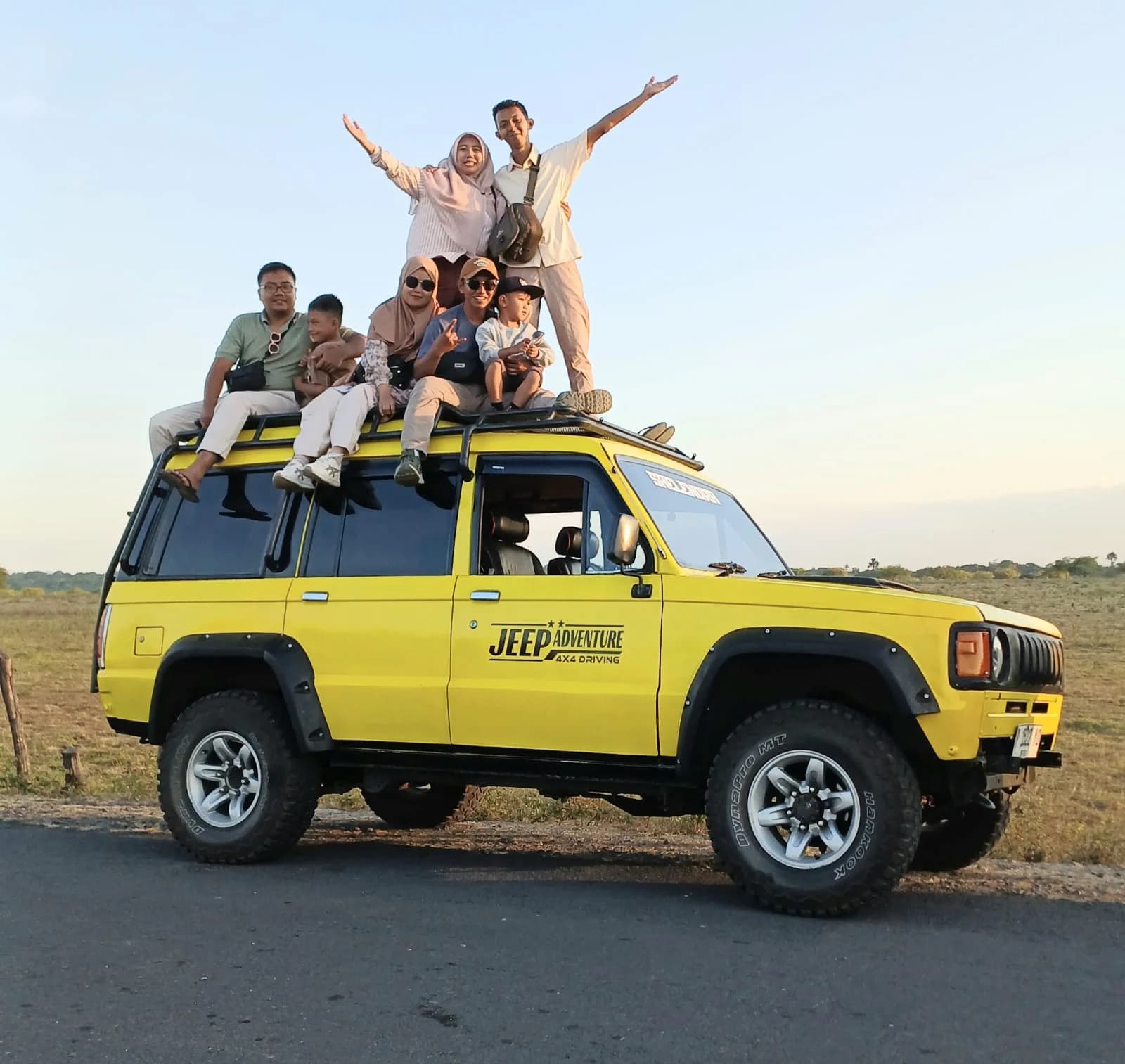 Wisatawan berfoto seru di atas atap Jeep Kuning Baluran dengan latar Savana Bekol dan Gunung Baluran