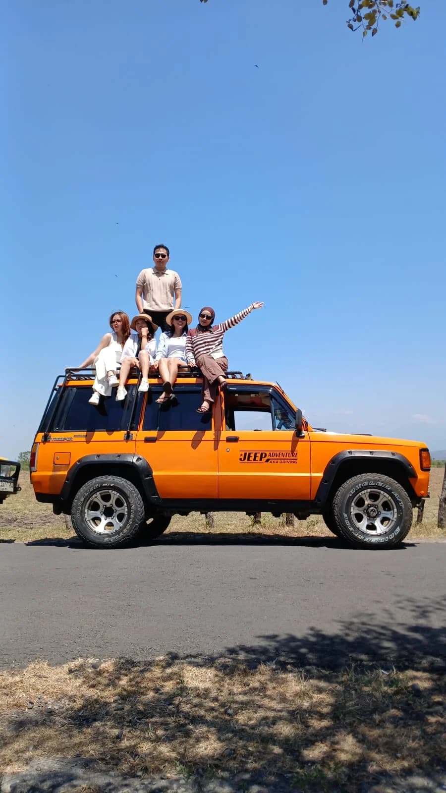 Jeep 4x4 oranye safari melintasi jalur makadam savana Baluran